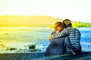 Ein Paar, dass auf einem Steg sitzt und sich umarmt. Menschen mit der Liebessprache Zärtlichkeit, fühlen sich durch eine Umarmung oder zärltiche Berührung geliebt.